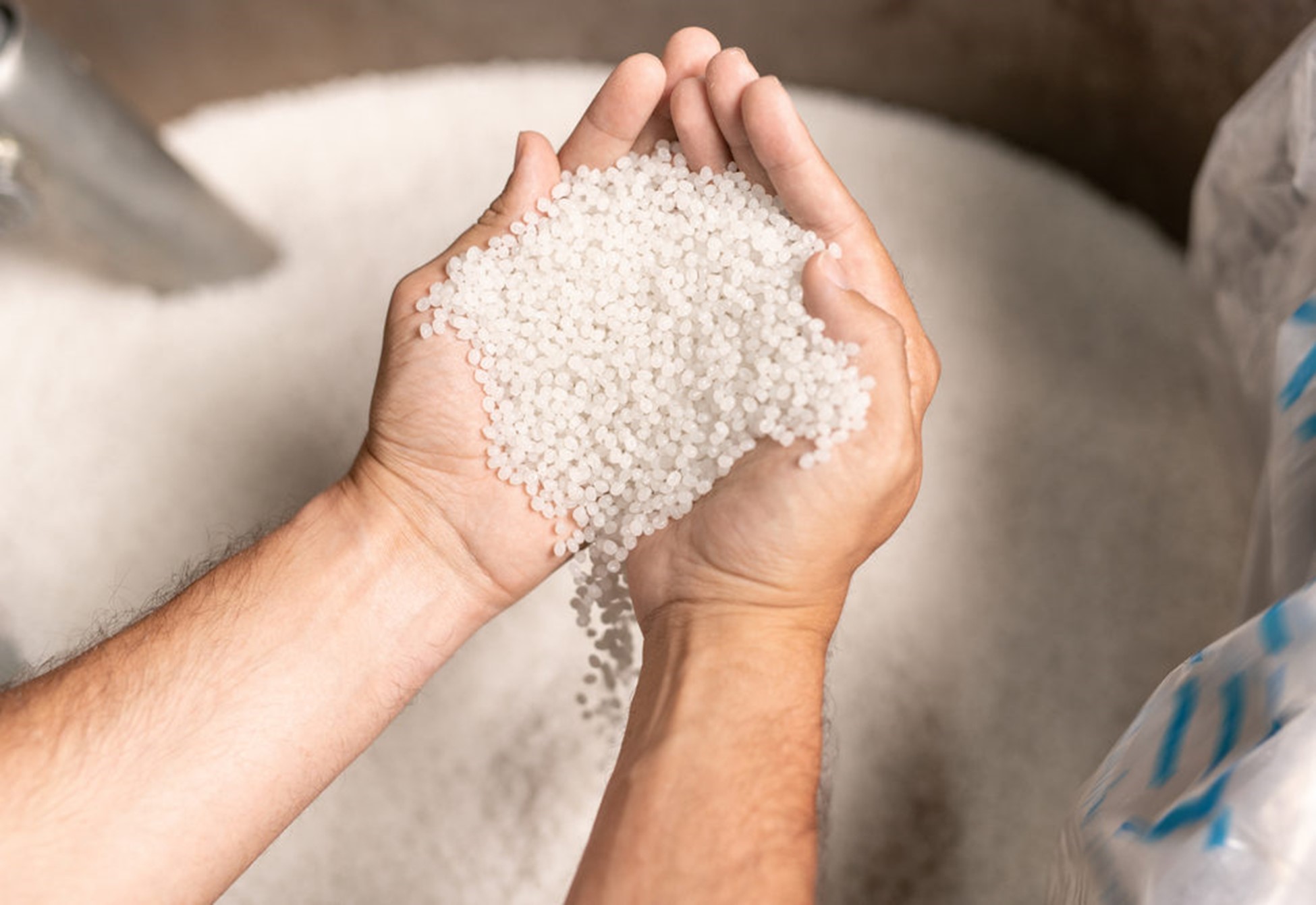 factory worker hands holding pile of white polymer pellets