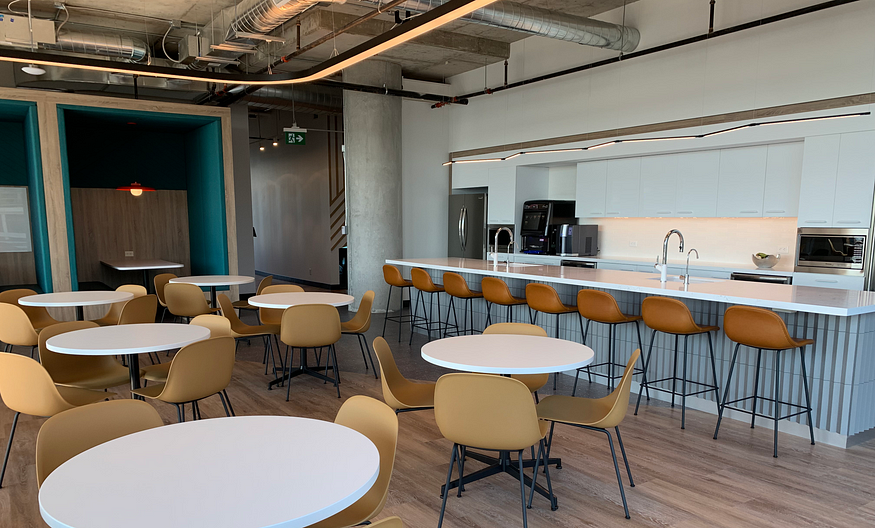 Office cafeteria showing café tables, banquettes, and counter stools with different light fixtures hanging from ceiling.