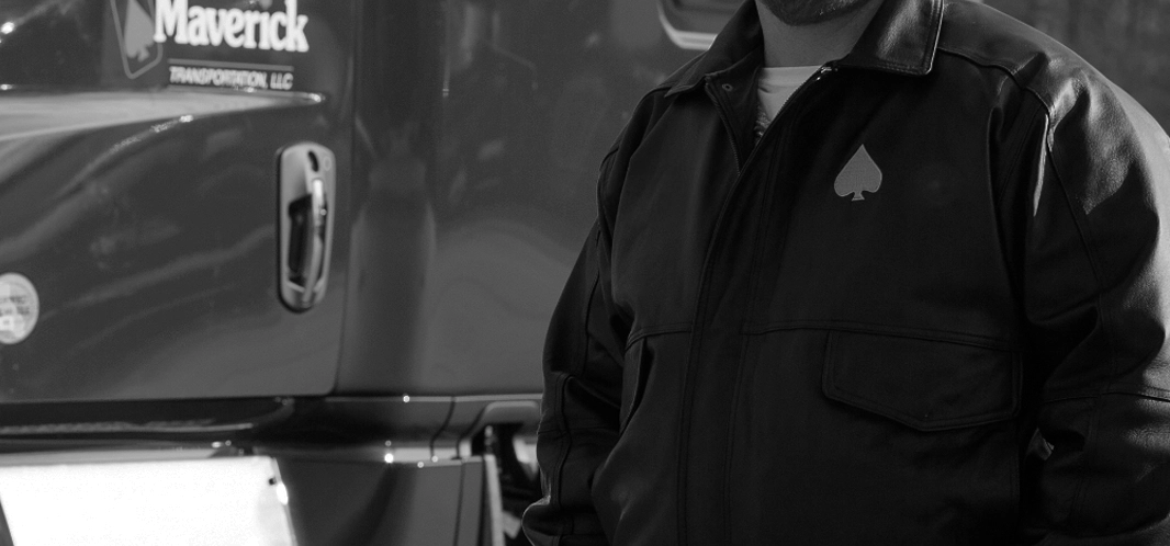 A man standing in front of a truck wearing a black leather Driver of the Year jacket