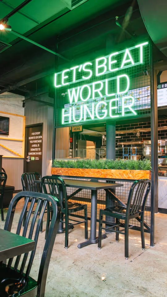 Inside Zambrero location with neon Lets Beat World Hunger sign
