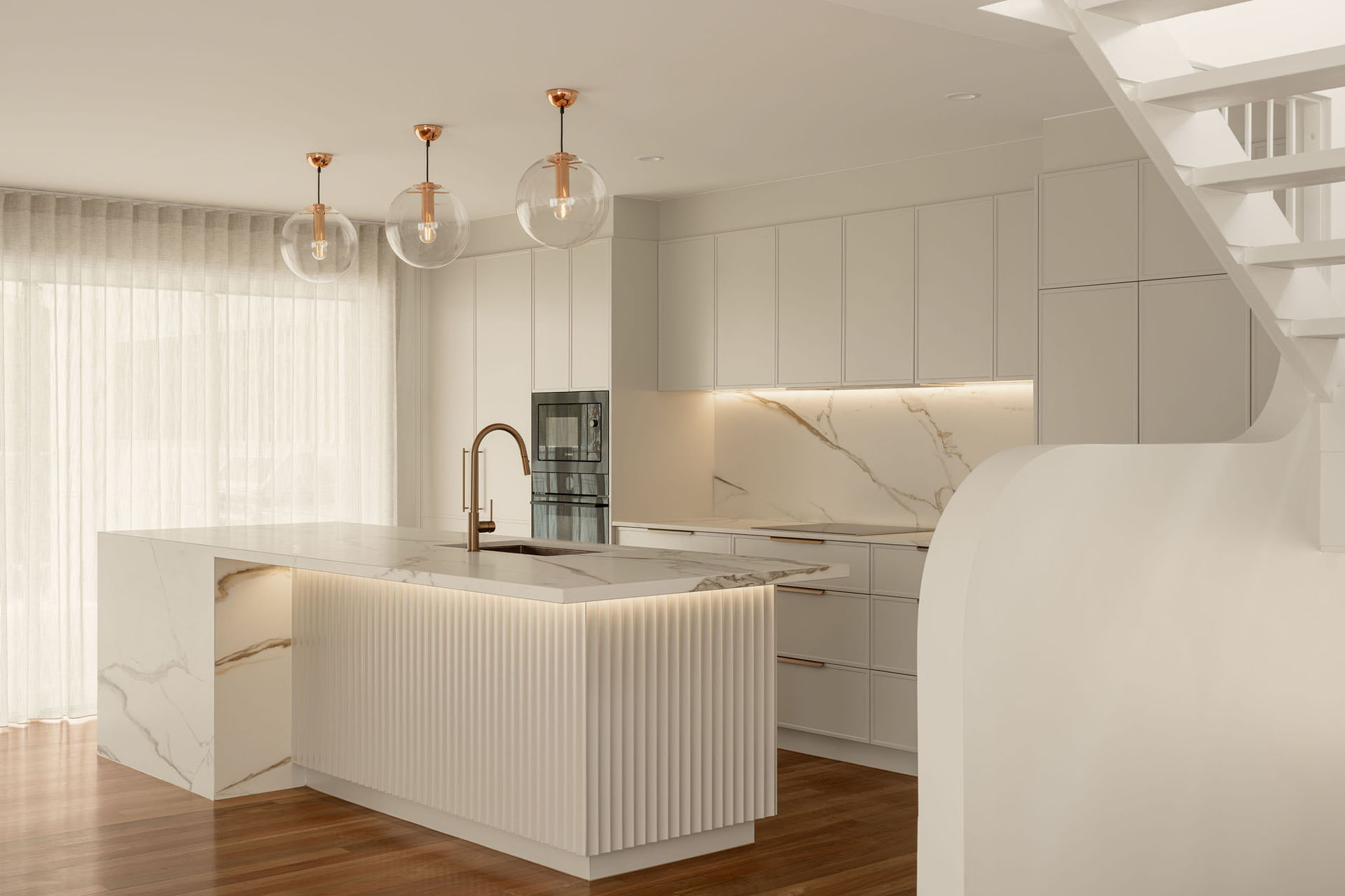 Modern kitchen with marble countertops, a central island with gold faucet, under-cabinet lighting, and three glass pendant lights.