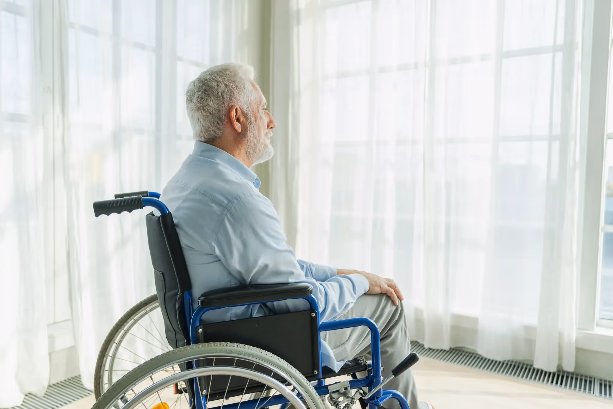 Elderly man in wheelchair looking out nursing home window symbolizing neglect