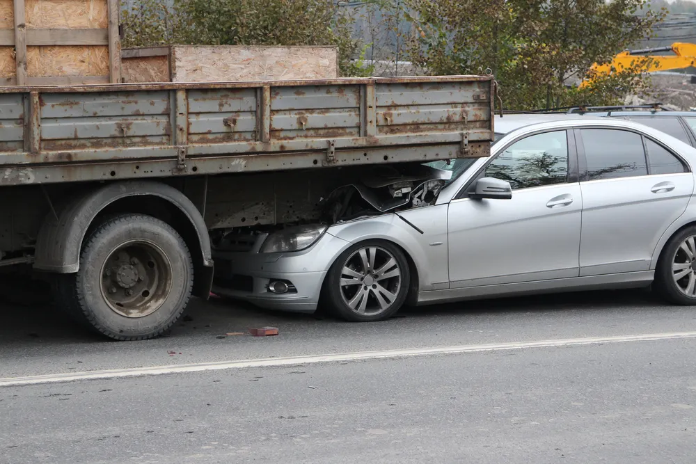 Car lodged underneath the rear of a flatbed truck after an underride accident