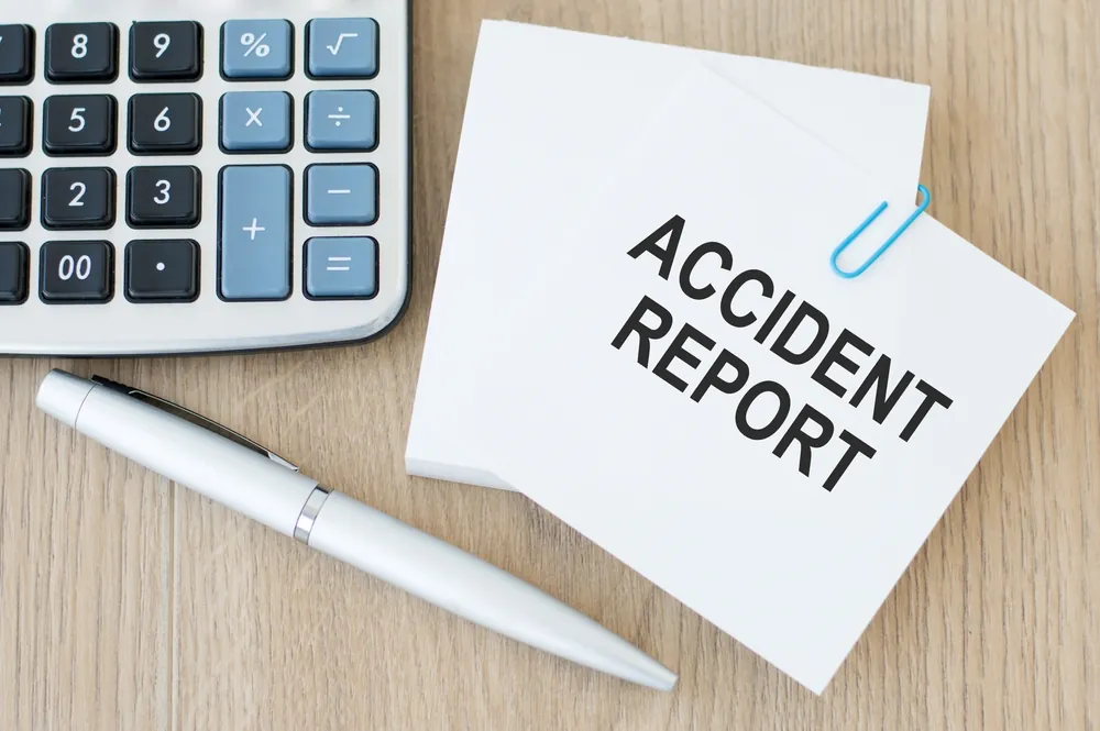 Accident report note beside a calculator and pen for estimating a Georgia car accident settlement