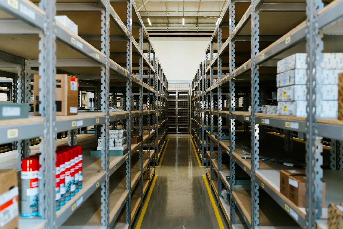 Warehouse interior with metal shelves lined with boxes and cans, creating a neat, organized symmetry. Bright lighting and spacious aisles suggest efficiency.