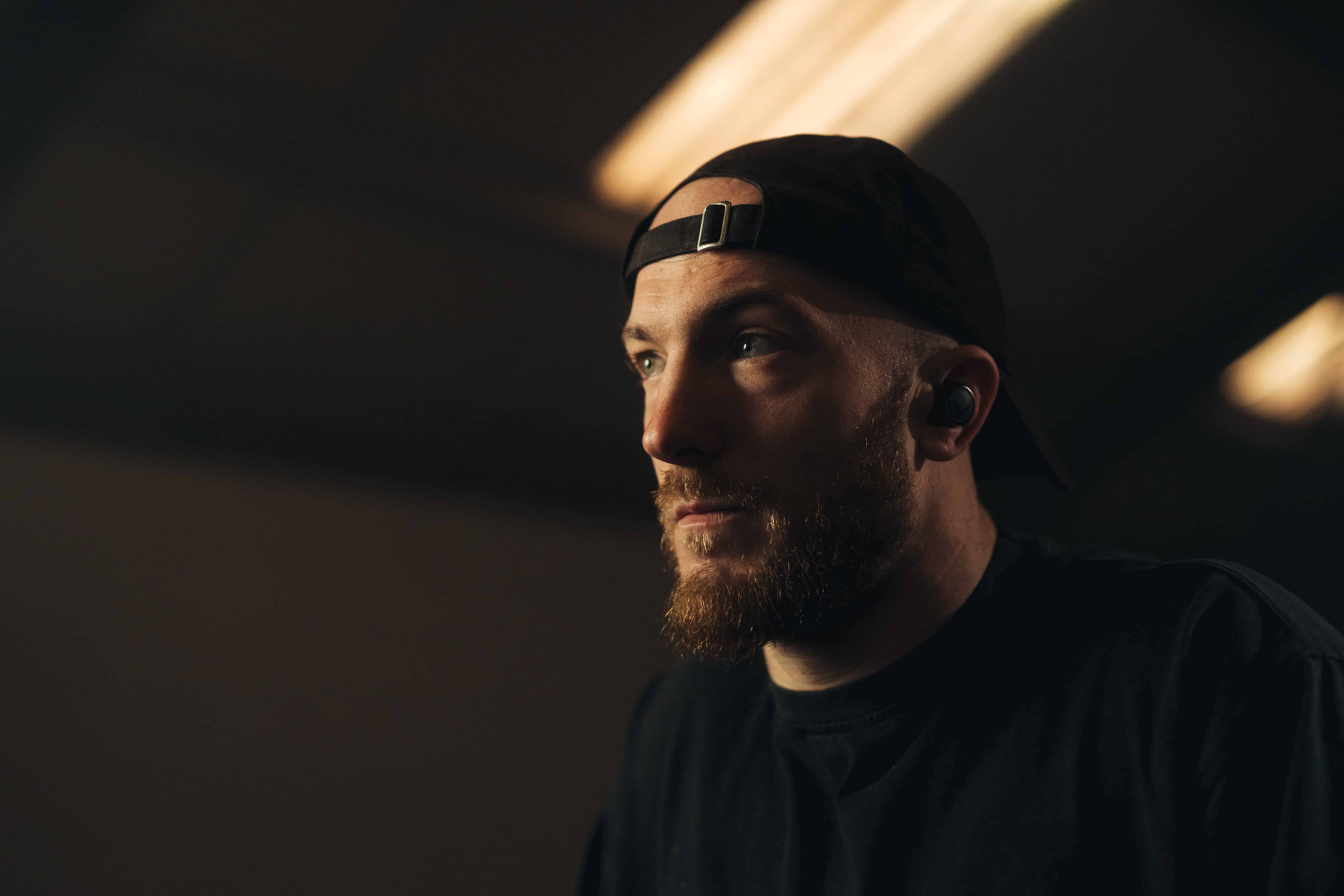Man wearing the best earbuds for running with a backwards cap and dark athletic wear, lit dramatically in a moody indoor setting