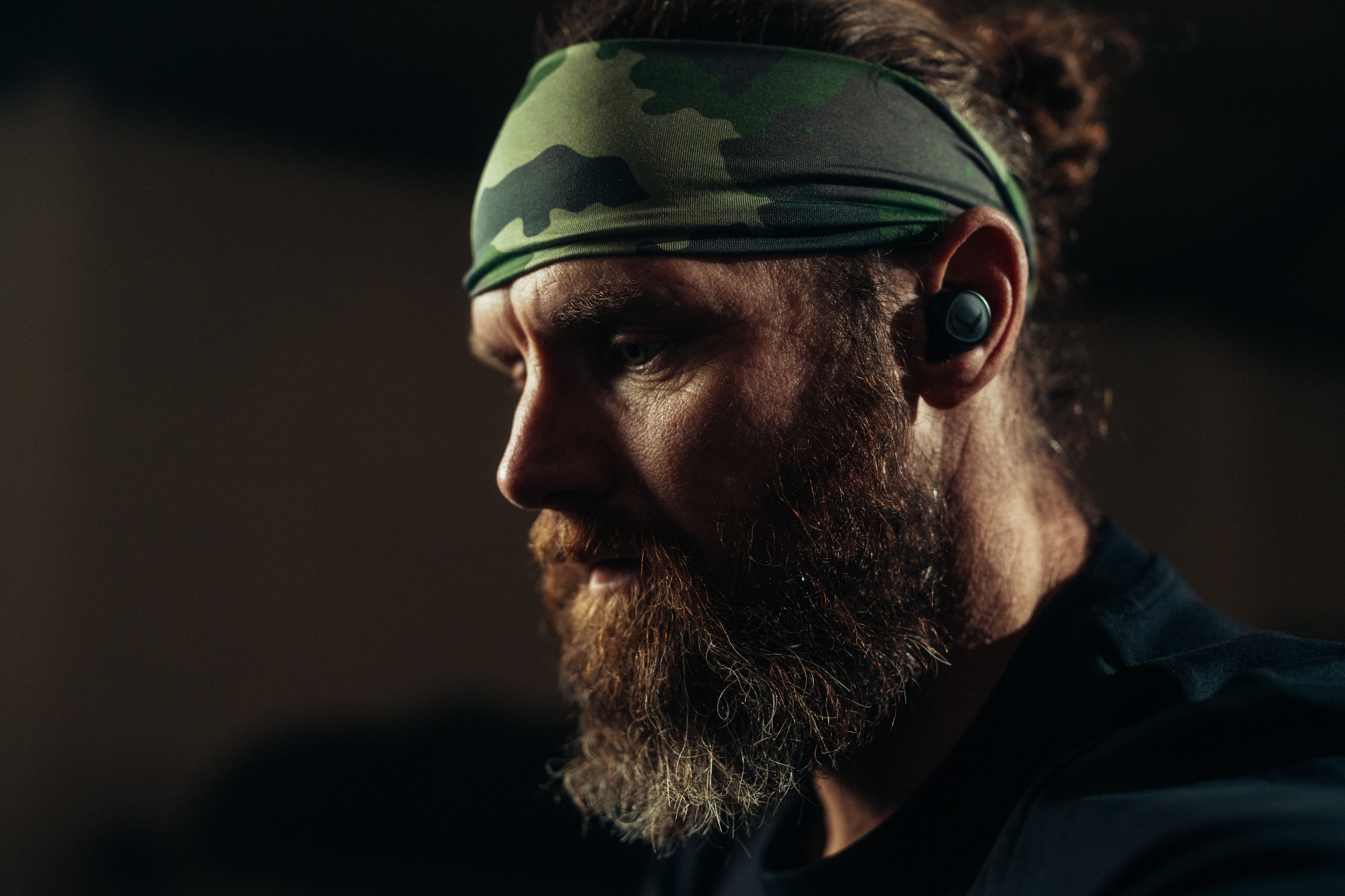 Bearded man wearing workout earbuds and camouflage headband during gym training session