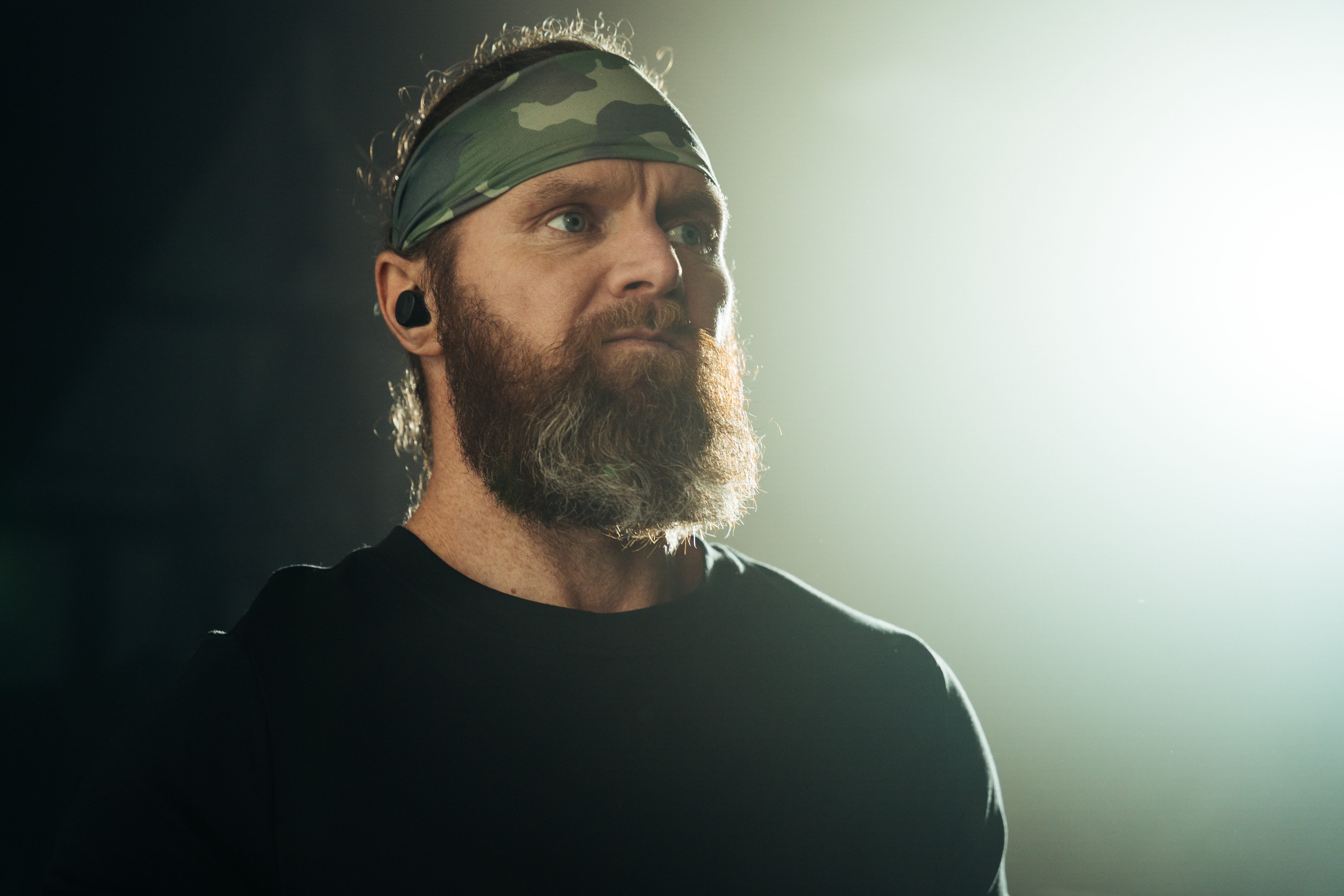 Focused male athlete wearing earbuds with mp3 player and camo headband, dramatic studio lighting portrait for workout and fitness use