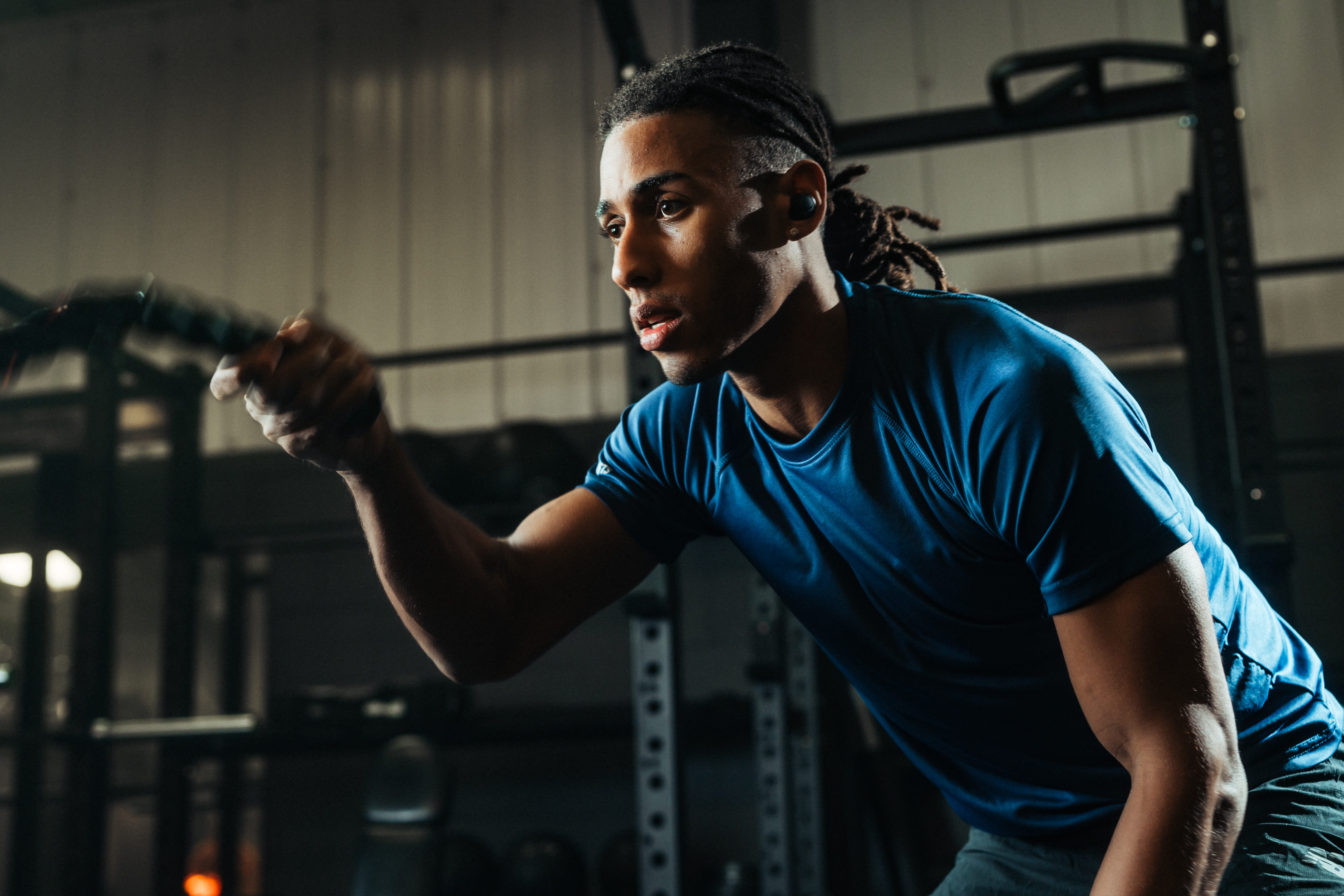 Athlete using phone-free workout earbuds during intense battle rope training session in gym