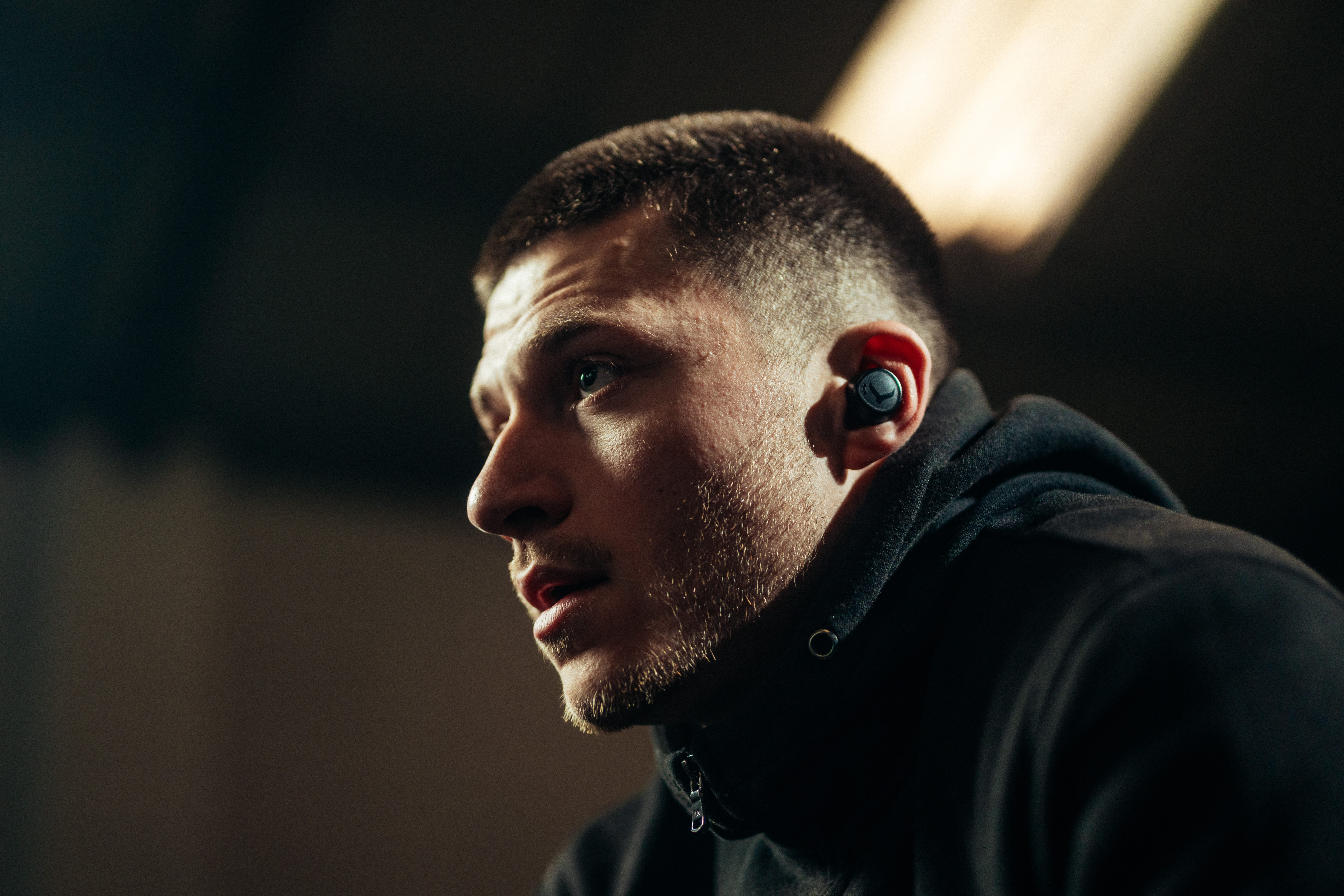 Man wearing phone-free workout earbuds in close-up portrait with dramatic studio lighting