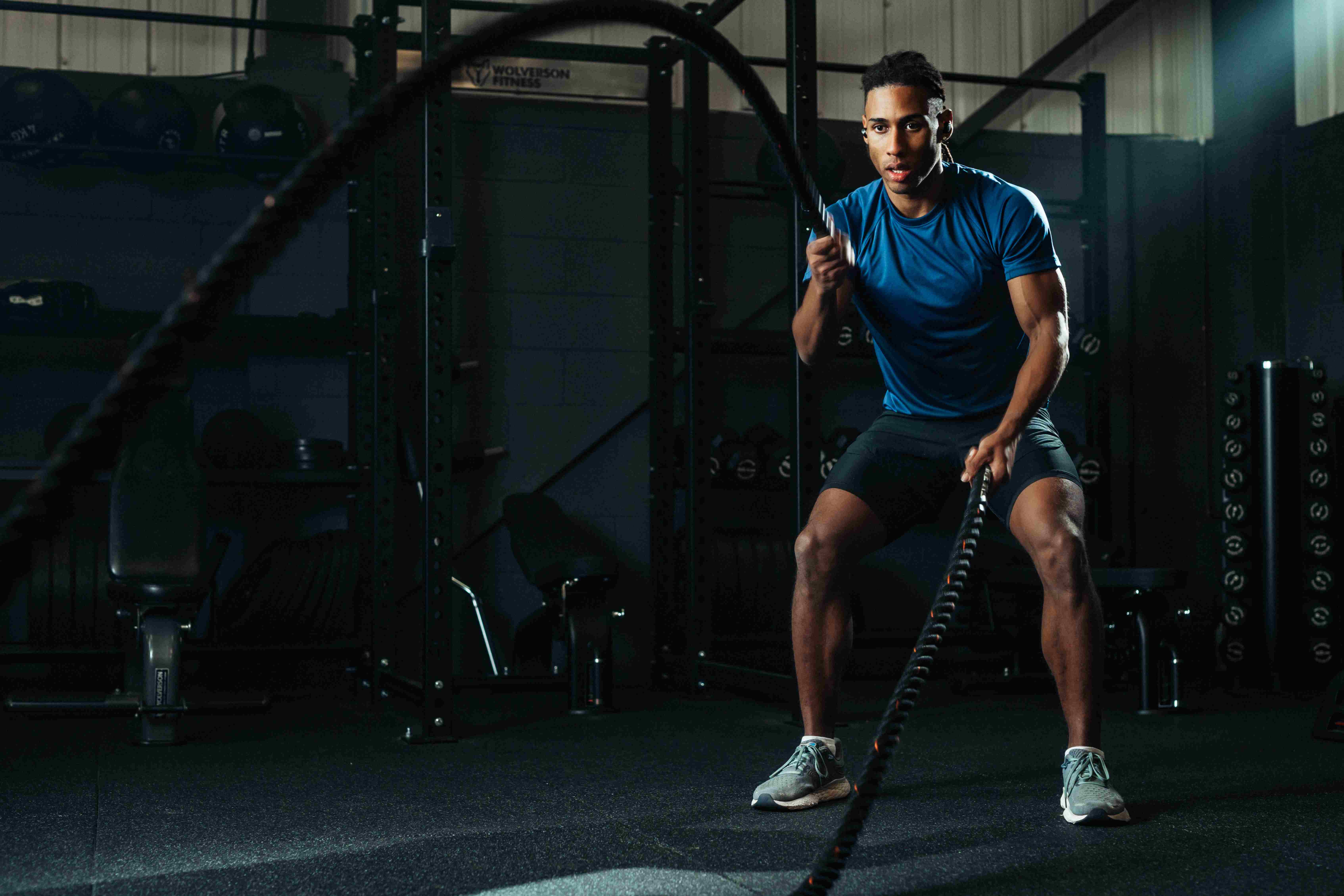 Hybrid athlete training with wireless workout earbuds during a battle ropes conditioning session