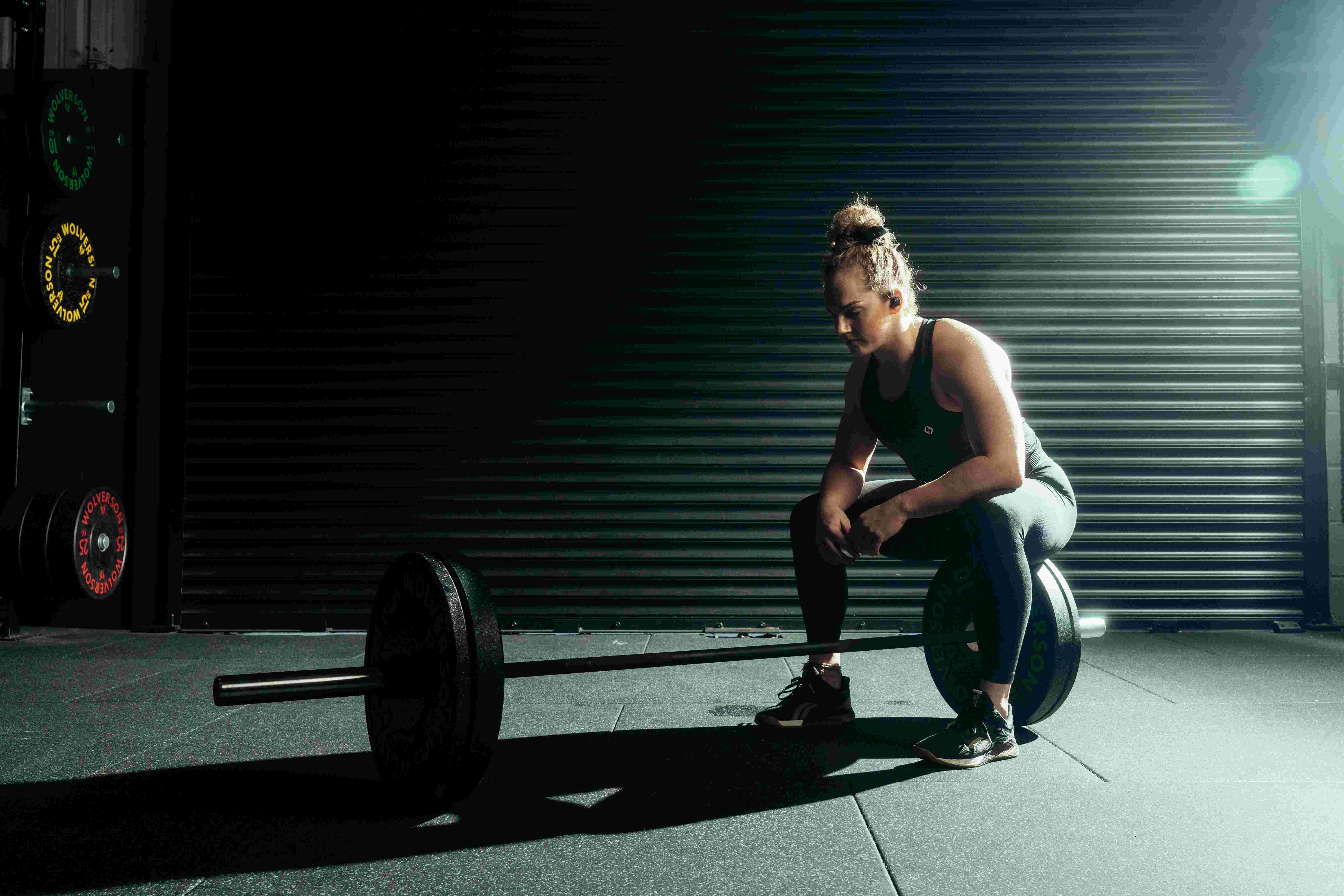 Lifter resting on a loaded barbell wearing phone-free workout earbuds, no smartwatch needed