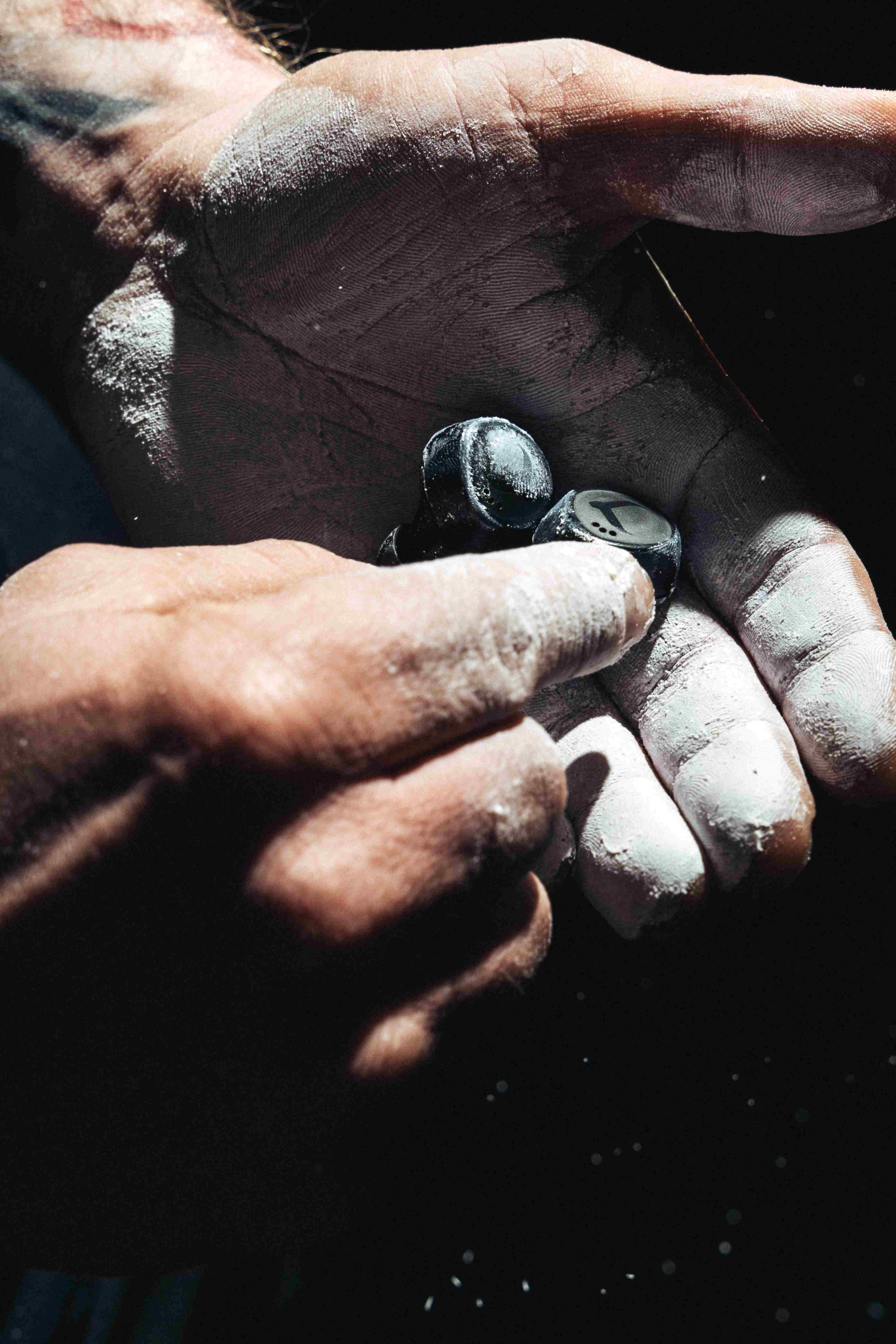 Chalked hand holding a single black Tzuka earbud after a lift