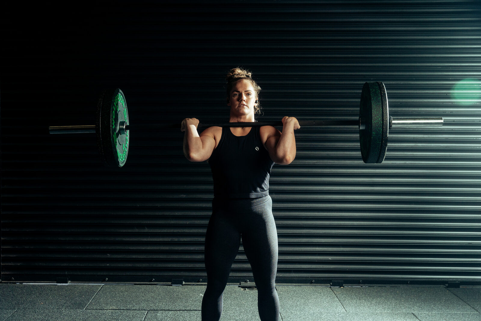 Athlete catching a clean in a CrossFit box wearing black Tzuka TZ7 Ultra earbuds