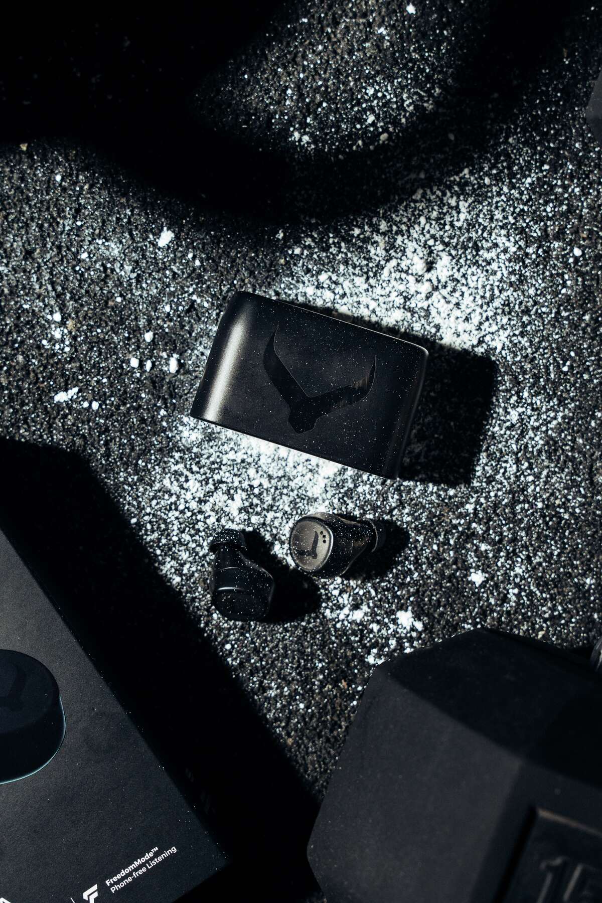 Tzuka TZ7 Ultra earbuds and charging case beside chalk and a dumbbell in a gym