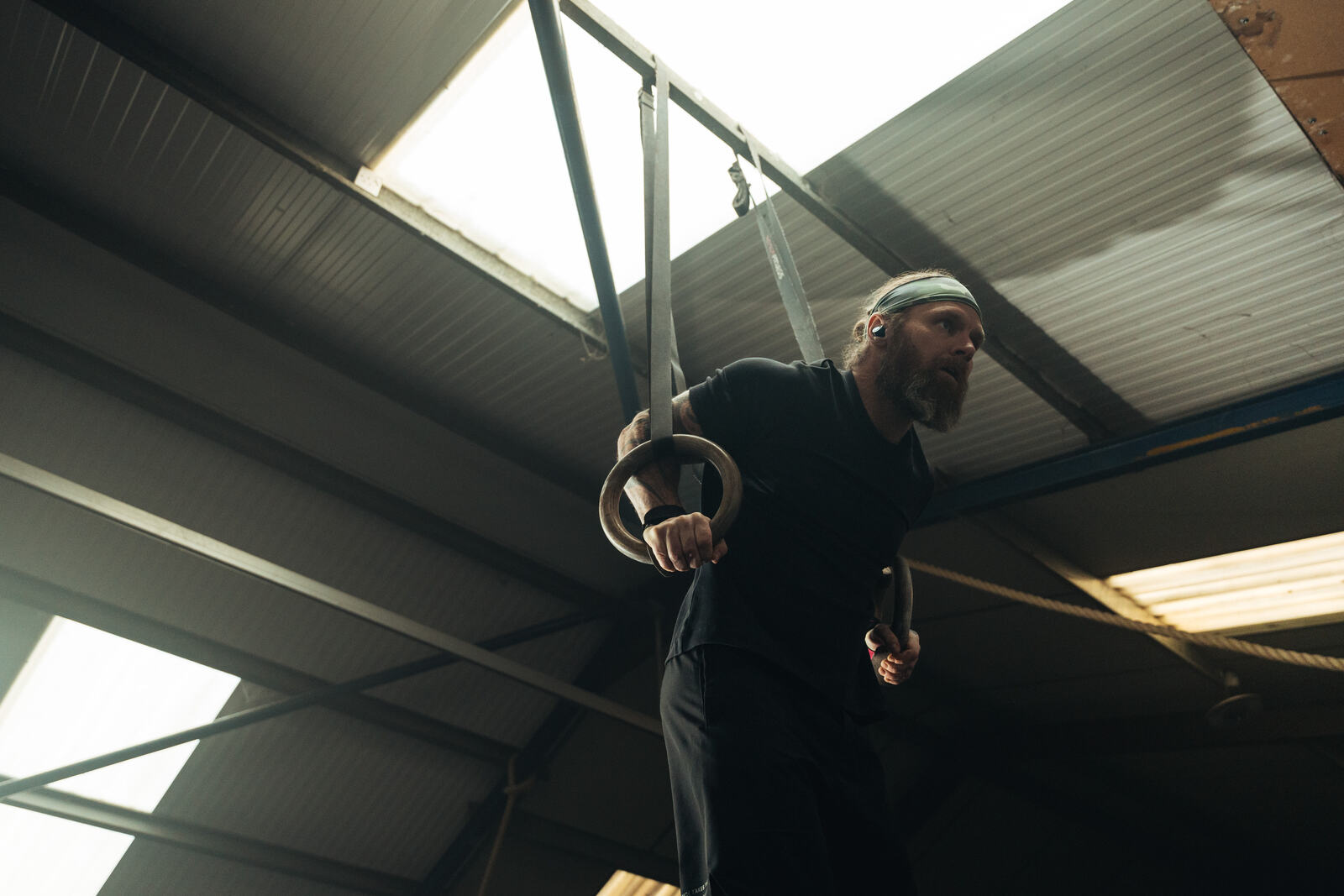 Athlete on gymnastic rings mid muscle-up wearing black Tzuka TZ7 Ultra earbuds