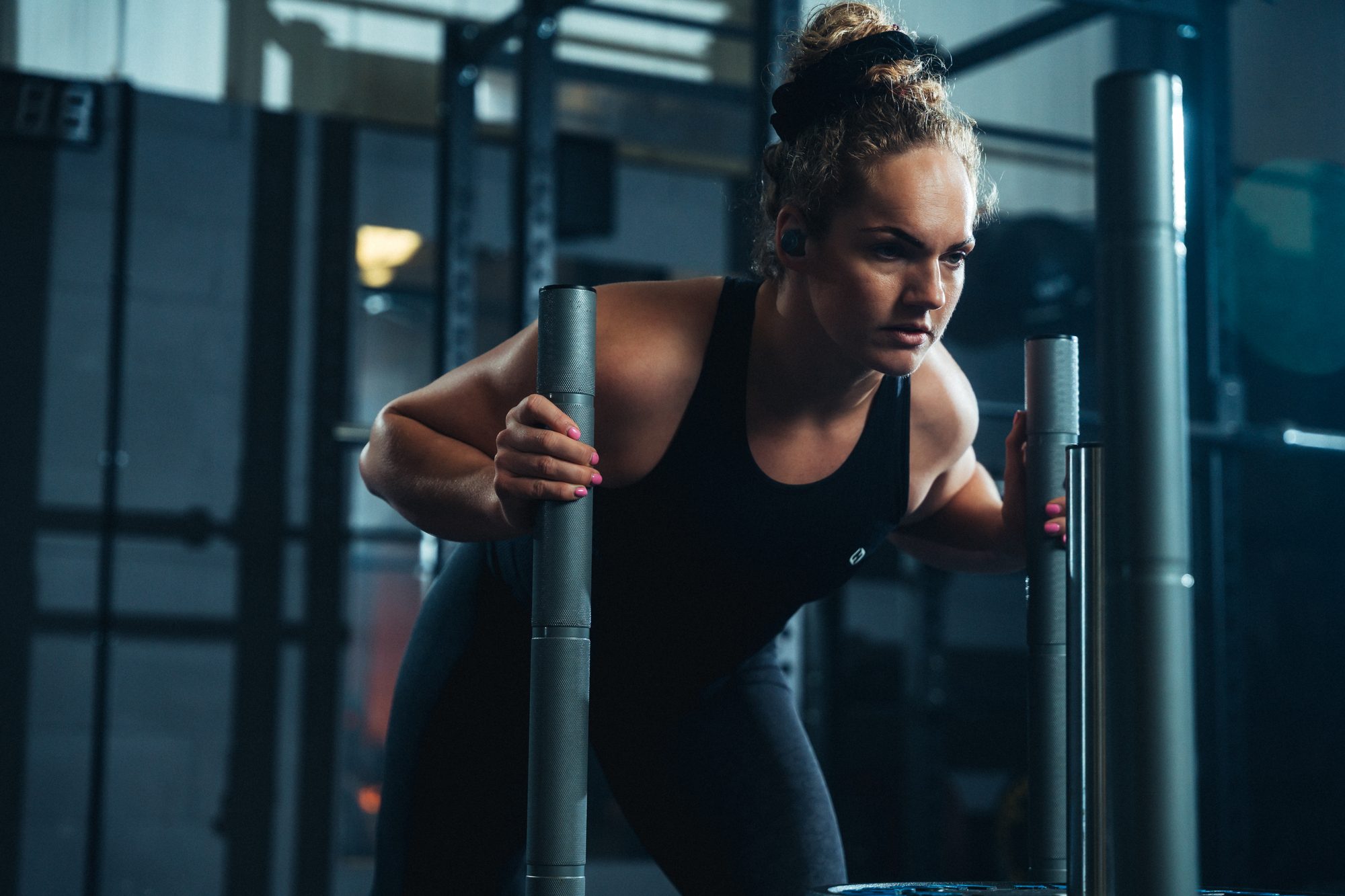 Female athlete leaning into a sled push in a gym, training for HYROX