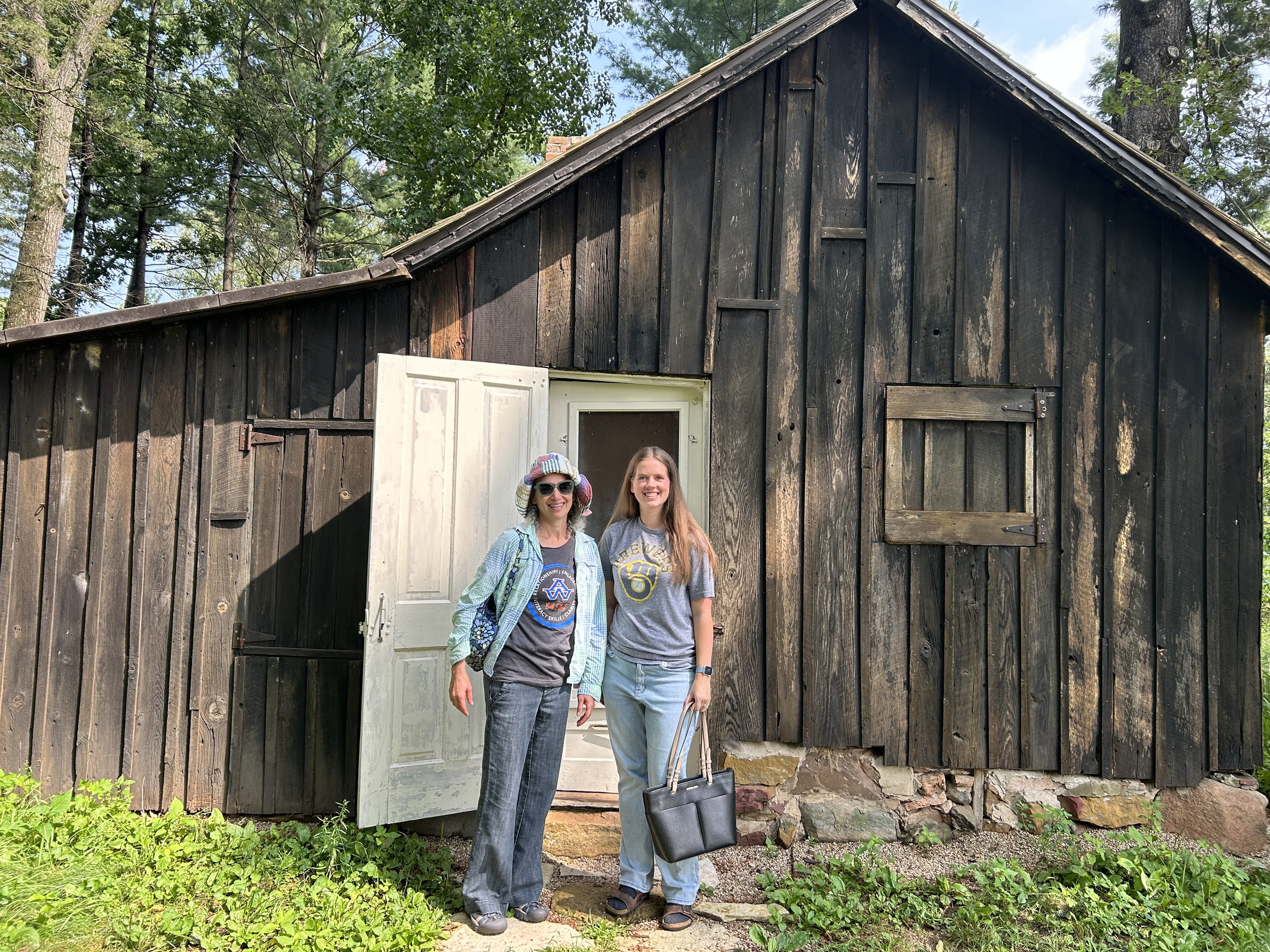 Two women stand in front of a rustic cabin