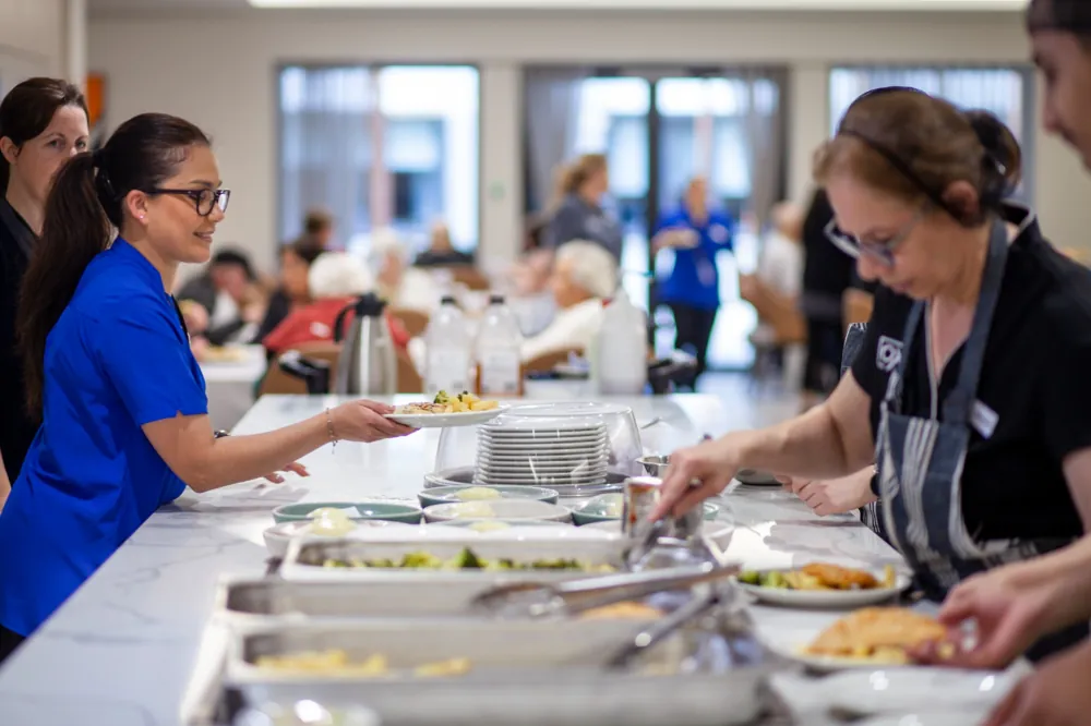 Multicultural dining experience at an aged care home, with staff serving diverse meals to residents.