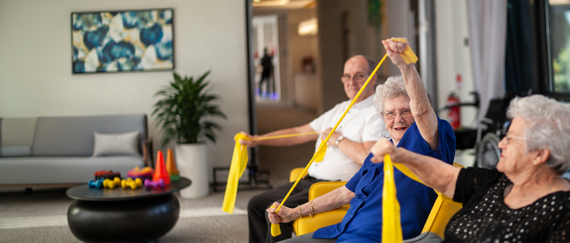 Oxa Care resident enjoying a seated resistance band exercise with other residents.
