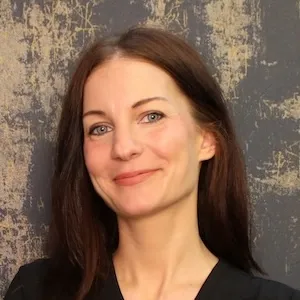 Woman with long brown hair smiling softly in front of a textured gray and beige background.