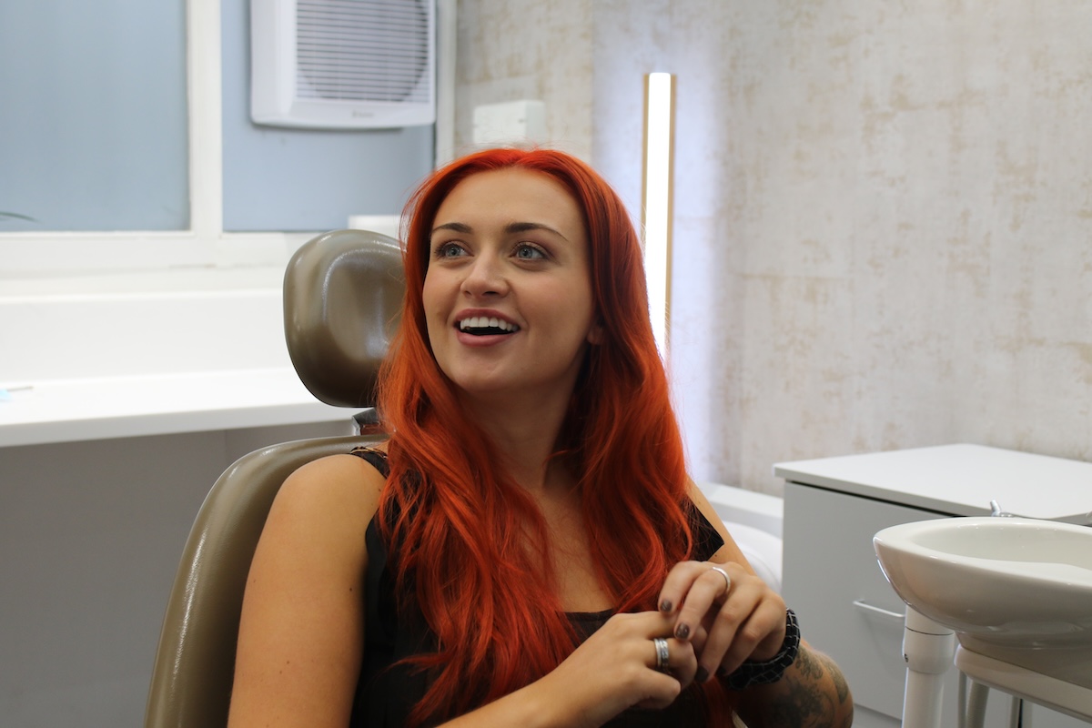 Smiling woman with long red hair sitting in a dental chair in a clinic.