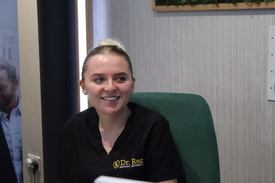 Smiling woman in black Dr. Rez dentistry uniform sitting on a green chair indoors.