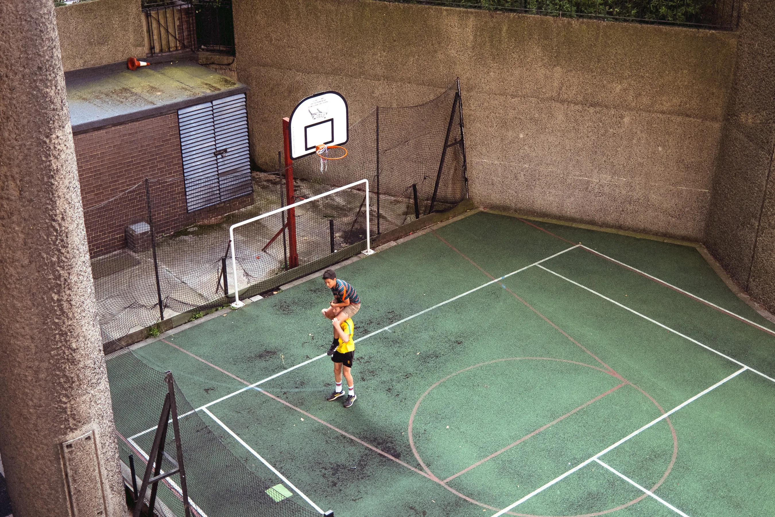 2 Youngs boys playing together on a green coloured basketball court. Shot on the Fujifilm x100v at the Barbican, London.