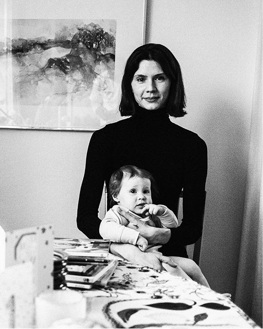 A mother holds her young child at a table in a Stockholm home, partially framed by pale tulips in the foreground.
