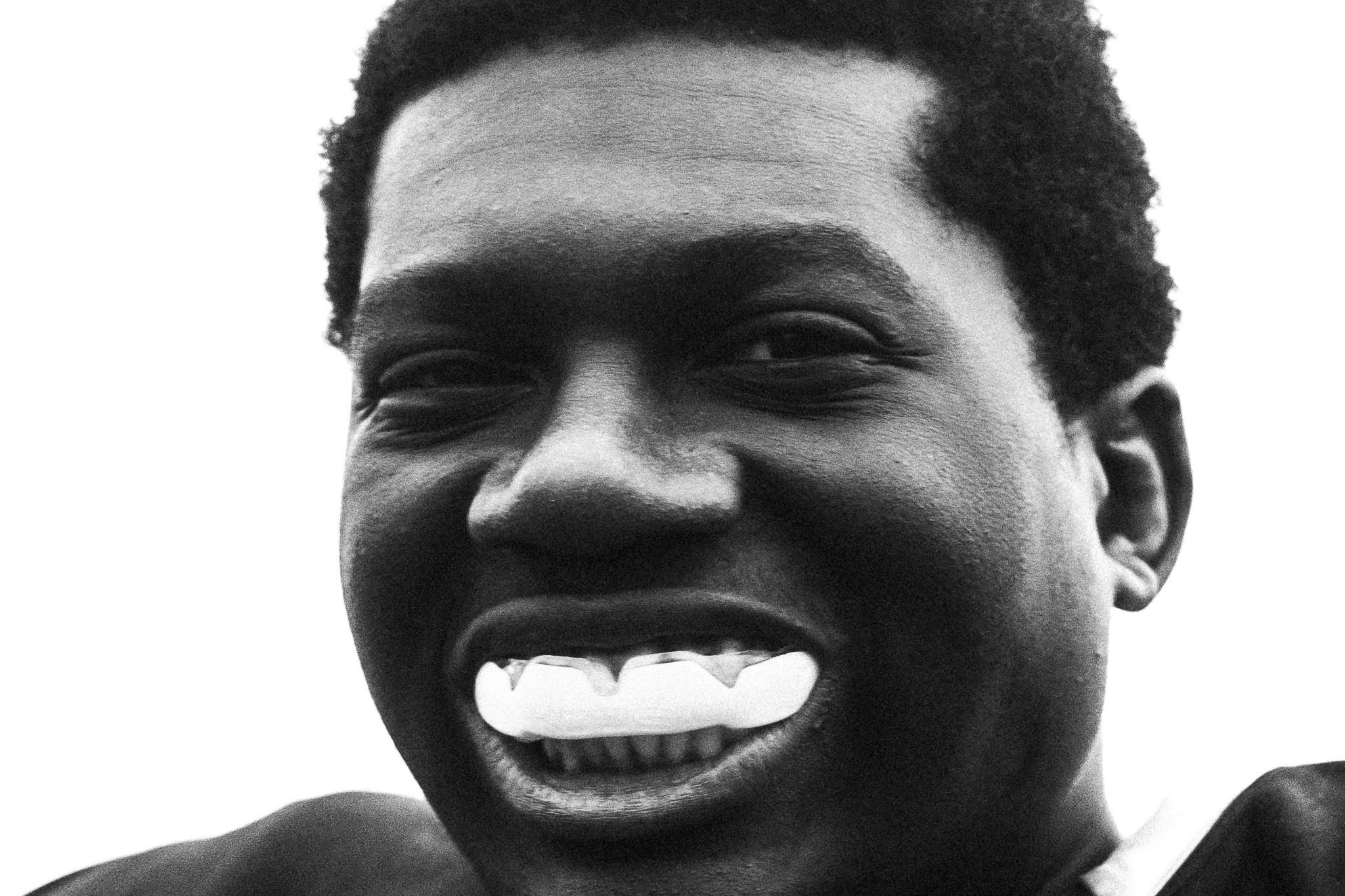 Close-up black-and-white portrait of an Anglia Ruskin Siege American football player smiling with a mouthguard in Cambridge.