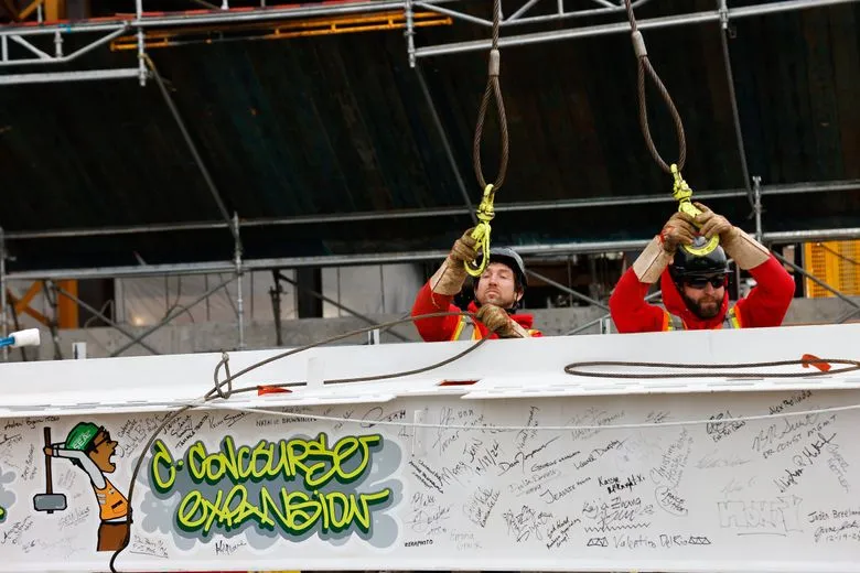 Ironworkers rig one of the final steel beams that bears the signatures of people who worked on the C Concourse Expansion Project during a “topping out” ceremony at Sea-Tac Airport on Thursday. Turner Construction Company and Apex Steel used a crane to put the beam in place atop the highest point. (Karen Ducey / The Seattle Times)