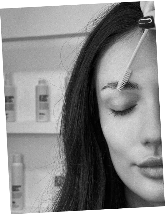 Close-up of a woman grooming her eyebrow with a spoolie brush, eyes closed.