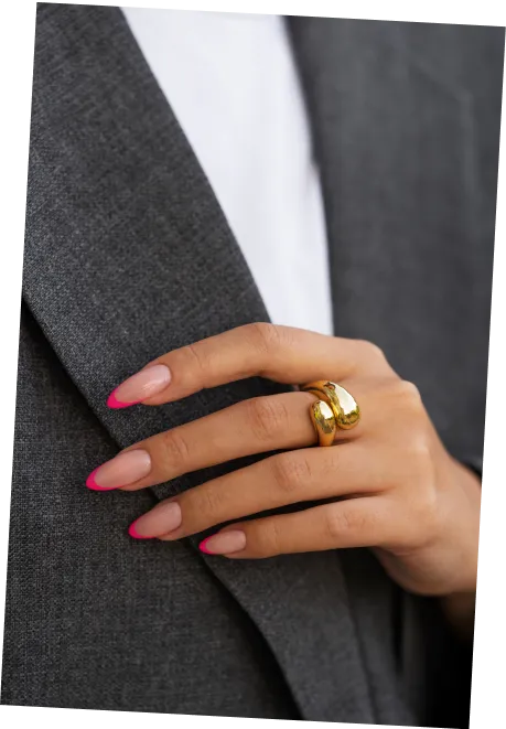 Hand with pink-tipped nails and thick gold ring resting on gray blazer fabric.