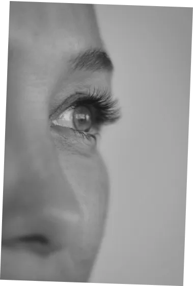 Close-up profile of a person's eye with long eyelashes looking into the distance in black and white.