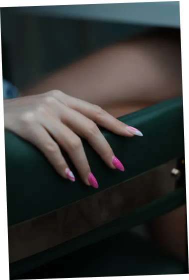 Hand with pink and white nail art resting on a green chair's backrest.