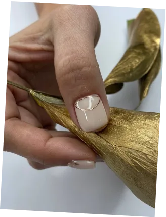 Close-up of a hand with nude nail polish holding a gold-painted dried leaf.