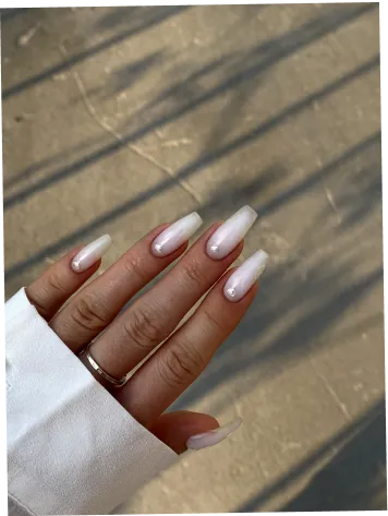 Hand with long, square-shaped French manicure nails and small decorative gems on a neutral background.
