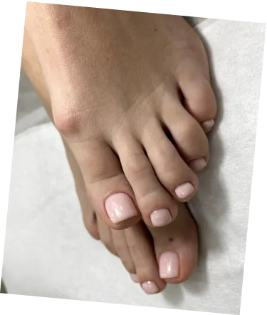 Close-up of feet with pale pink polished toenails on a white surface.