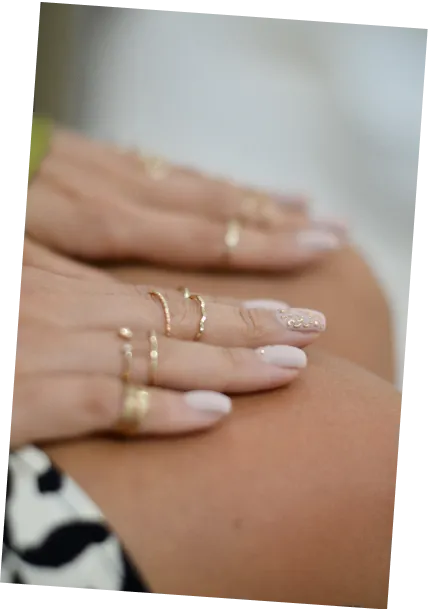 Two hands with manicured nails and gold rings resting on bare knees.