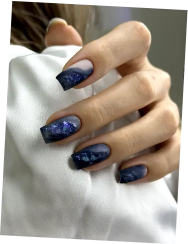 Hand with long square nails painted navy blue with shiny foil accents on white fabric background.