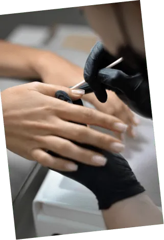 Person wearing black gloves applying nail polish to another person's fingernails in a manicure.