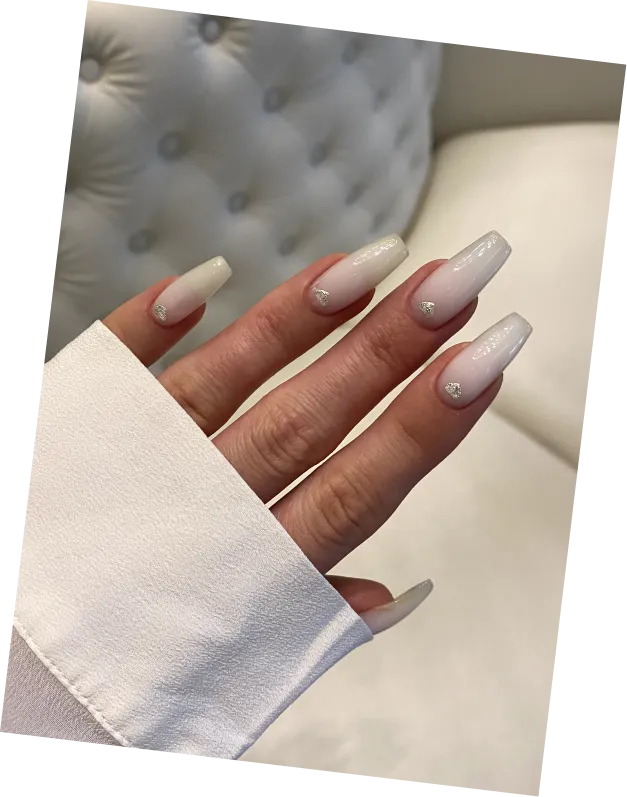 Hand with long, glossy white ombré nails decorated with small silver heart accents near cuticles.