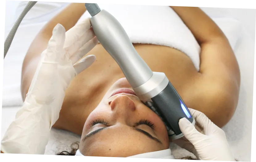 Woman receiving a facial treatment with a handheld skincare device by a gloved professional.