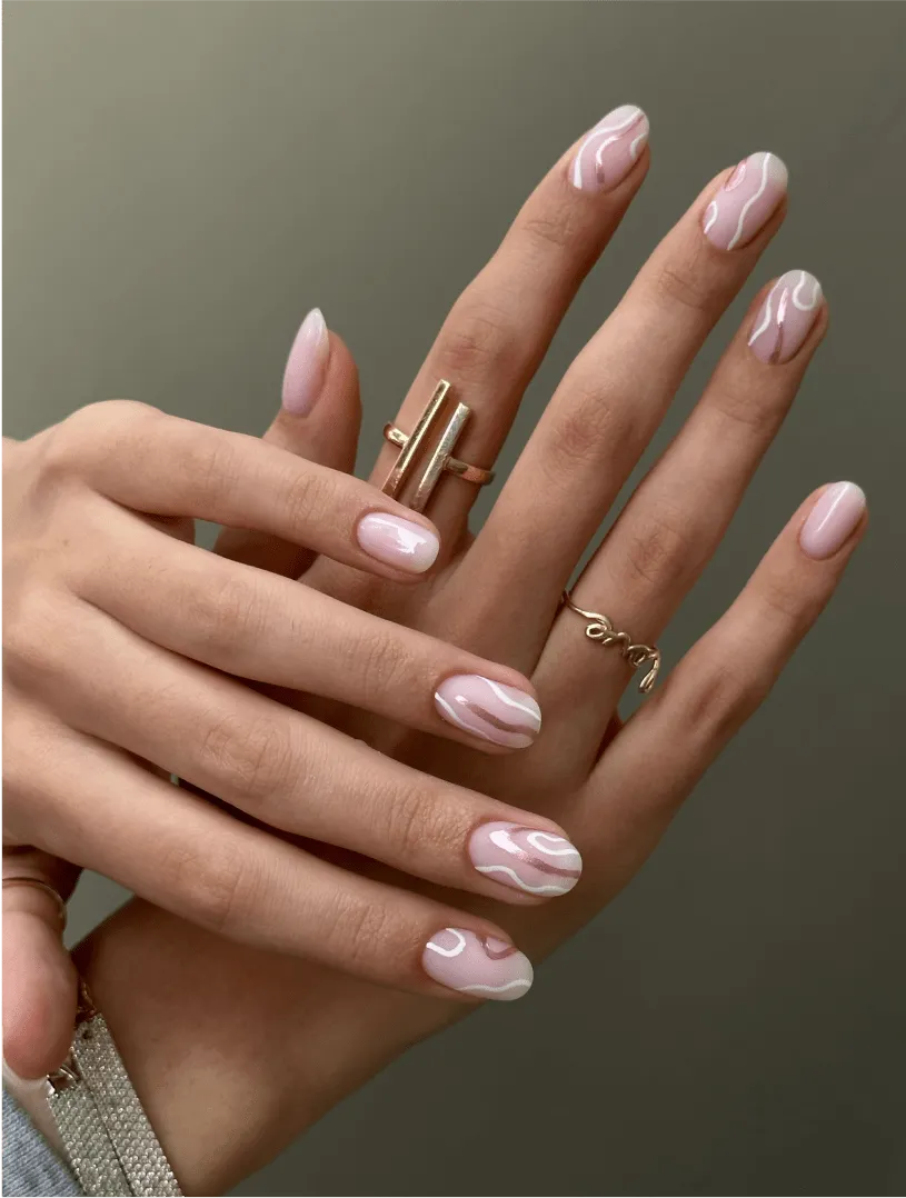 Two hands with pale pink manicure with white abstract swirls and gold rings on fingers.