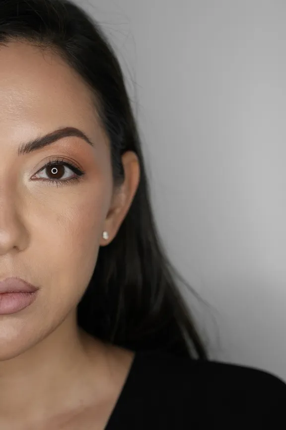 Close-up of a woman's face showing brown eyes, natural makeup, and dark hair against a gray background.