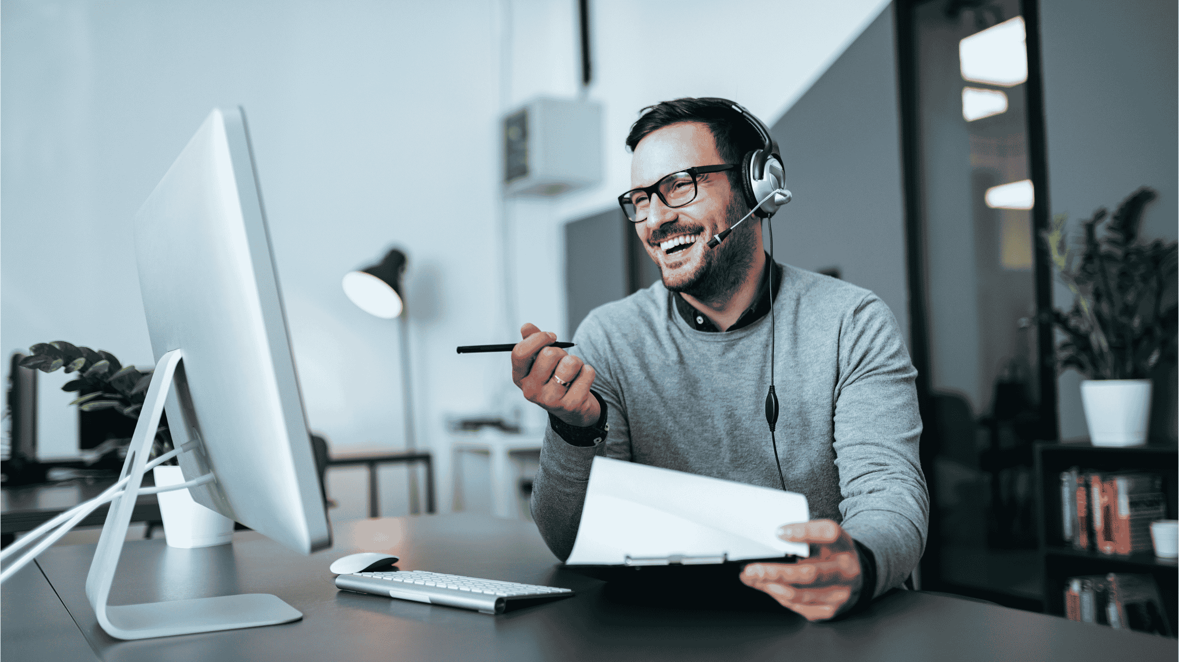 A man in a modern office, wearing a headset and making a sales call.