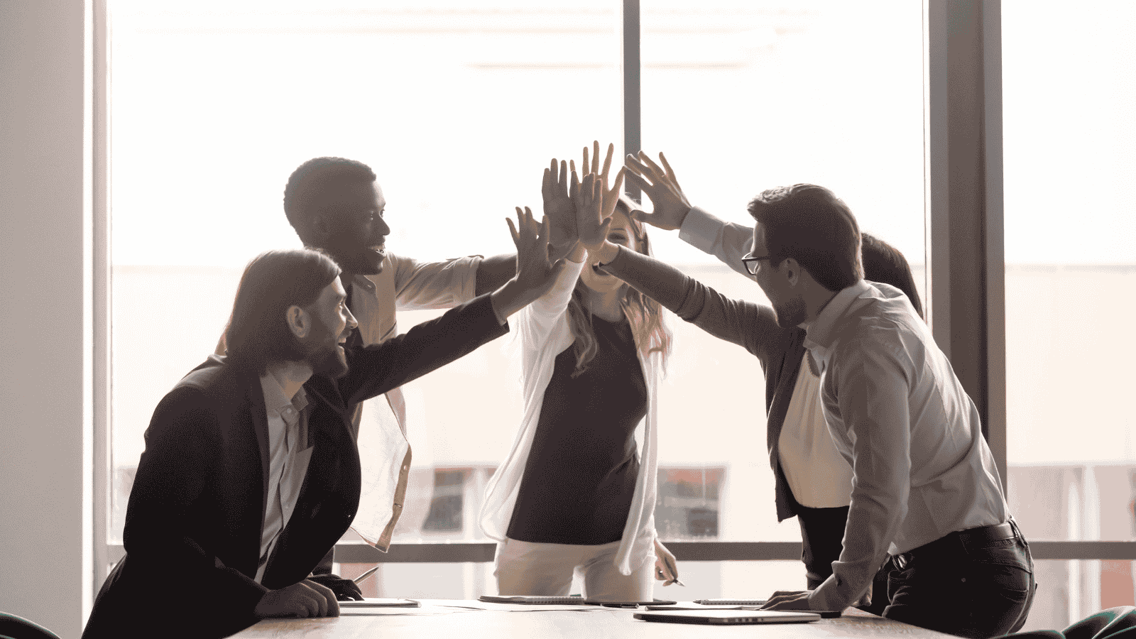 Diverse business team celebrating success with high fives, symbolizing cross-functional collaboration and revenue alignment