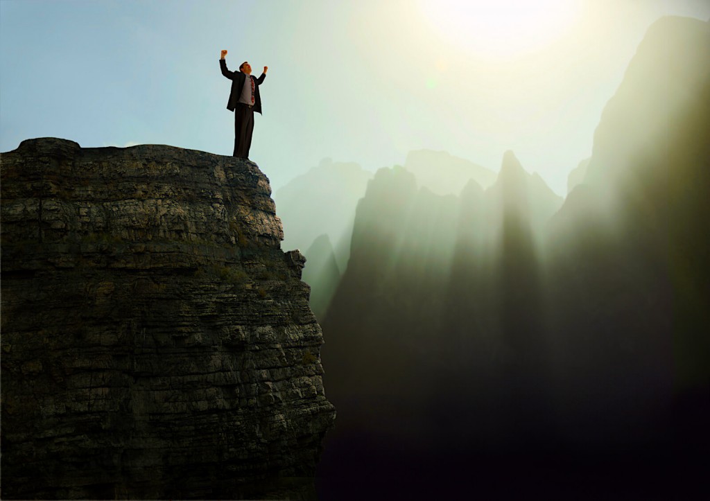 A man on top of a cliff, reaching his arms toward the sky.