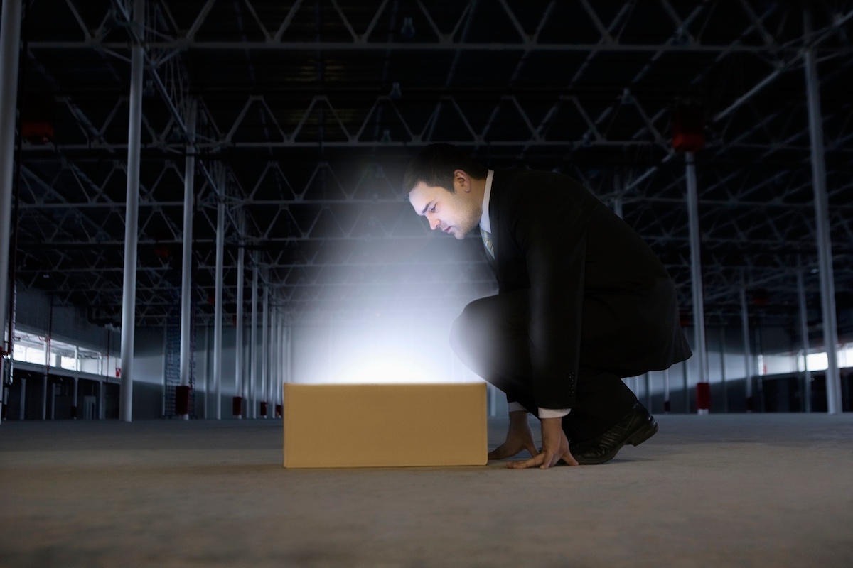 A business man in a warehouse peering into a glowing box.