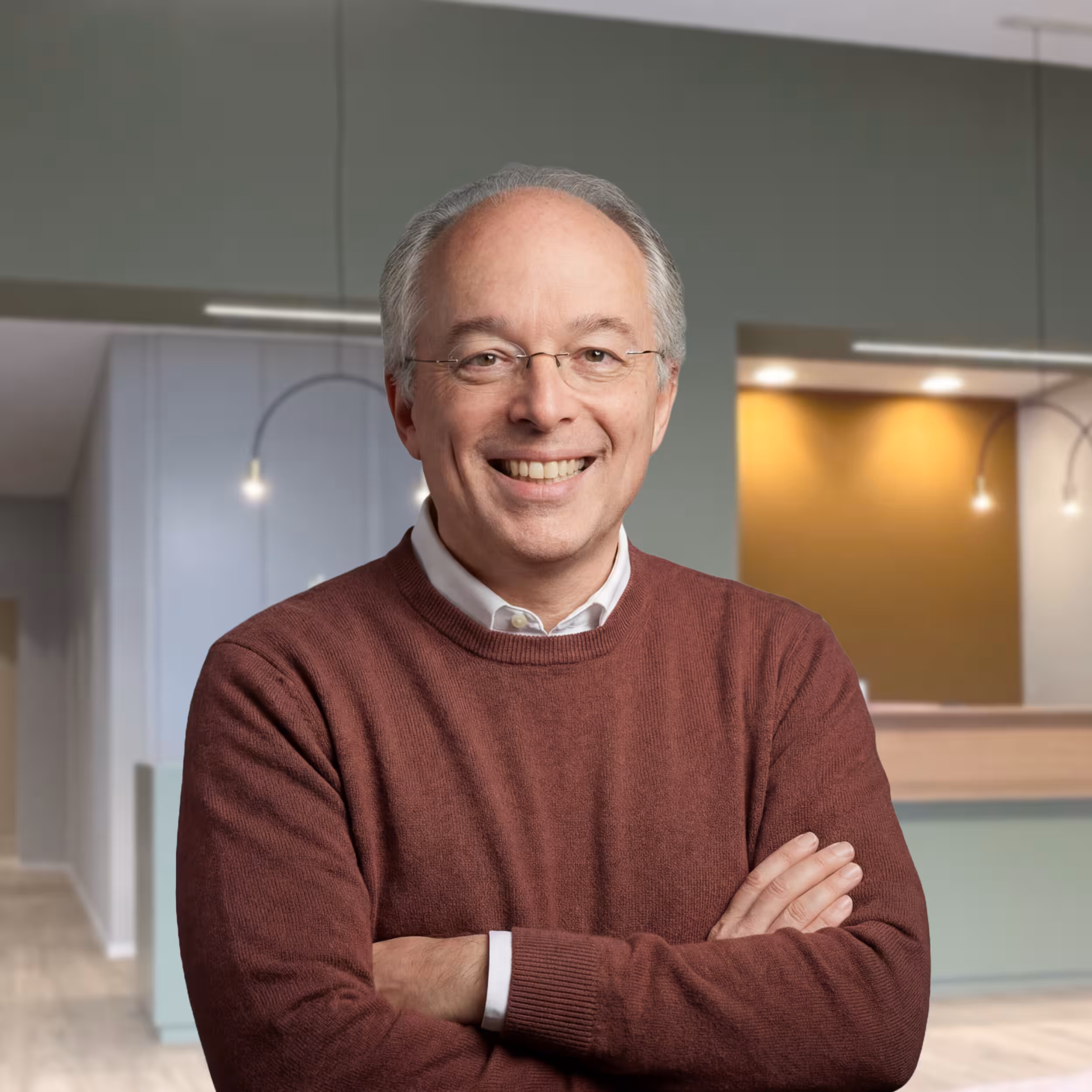 Doktor Gorsler steht in einen dunkelroten Pullover gekleidet, mit verschränktem Armen und einem warmen Lächeln in seiner Praxis für Kinderchirurgie in der Seestraße 98 13353 Berlin.